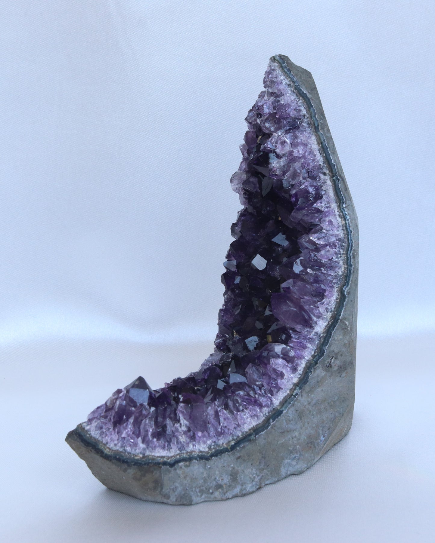 Dark purple amethyst sculpture moon shape with raw points, photo taken from the side.